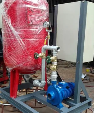 Bình tích áp đỏ nối với máy bơm xanh và tủ điều khiển trên khung thép